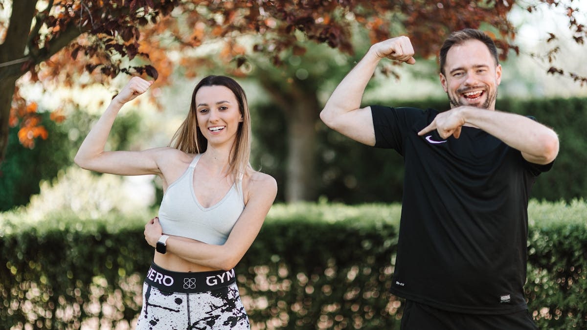 A cheerful couple posing outdoors in activewear, showcasing fitness and well-being.